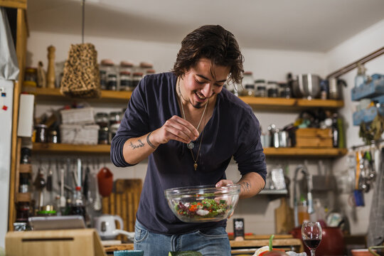 man seasoning salad in his kitchen