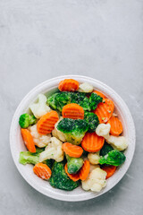 Frozen vegetables. Frozen carrots, broccoli and cauliflower in bowl on gray stone background