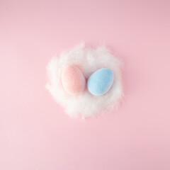 Easter scene with pink and blue egss in white feathered nest on pink background.