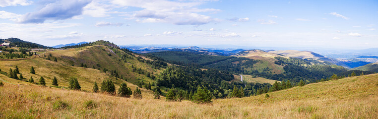 Fototapeta na wymiar Beautiful nature panoramic view of mountain range. Peaceful landscape. Green hills and fields on summer day. Blue sky with clouds. Panorama of Kopaonik mountain. Serbia. Europe.