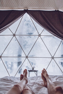 Legs of a man and woman couple in bed against the background of a snow-covered forest in a dome camping.