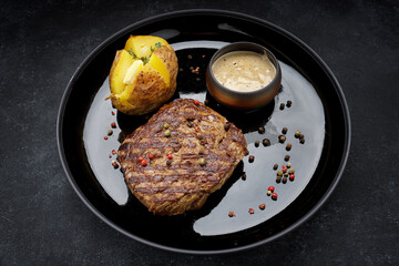 Grilled pork steak with baked potatoes, mustard sauce, pepper.