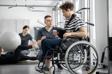 People doing exercises at rehabilitation center. Worker helps a guy in a wheelchair to do exercises...