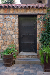Forged iron door in block wall with tiled visor. Tub with plants at entrance. Vertical photo.