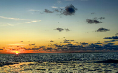 View of the setting sun shining on the Sea and reflected on the beach, clouds with sun-shining edges. Landscape. High quality photo