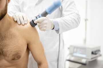 Doctor applies shock wave therapy with special medical equipment on shoulder of a young male...