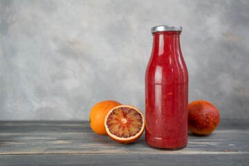 Bottle of blood orange juice with halved fruit on wooden table