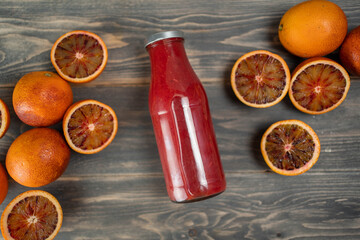 Bottle of blood orange juice with halved fruit on wooden table