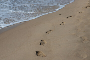 Footprints in the sand beach. Footprints in the sand against a sea wave. Footprints on a sunny day with golden sand, beach, wave and footsteps