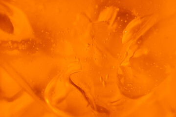 Fototapeta na wymiar Texture of transparent yellow gel with air bubbles and waves on orange background. Concept of skin moisturizing, body care and prevention of covid19. Liquid beauty product closeup. Backdrop, flat lay