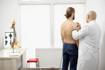 Athletic man on examination by physical therapist in medical office. Doctor examines patient's back...