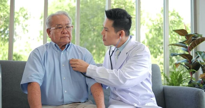 Asian man doctor use stethoscope to listen heart of elderly man patient. Nurse home visit, checking health of old senior grandfather, older people healthcare support concept.