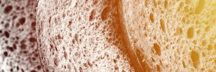 texture of slices white bread as close up background. gray backdrop of rough textured surface chopped pieces loaf of natural organic food with holes. top view. toned black white color. banner. flare