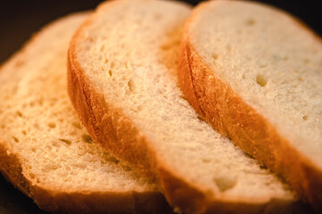 slices of white bread close up on a black background. rough dappled textured surface chopped pieces...