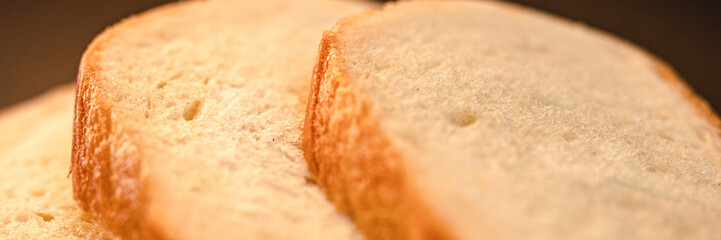 slices of white bread close up on a black background. rough dappled textured surface chopped pieces loaf of natural organic food with holes. banner