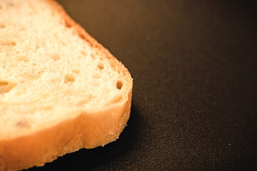 slice of white bread close up on a black background. rough dappled textured surface chopped piece loaf of natural organic food with holes