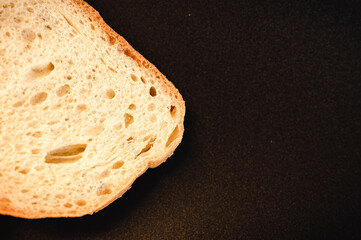 slice of white bread close up on a black background. rough dappled textured surface chopped piece...