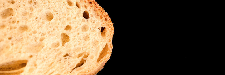 slice of white bread close up isolated on a black background. rough textured surface chopped piece loaf of natural organic food with holes. top view. abstract concept of the planet and space. banner