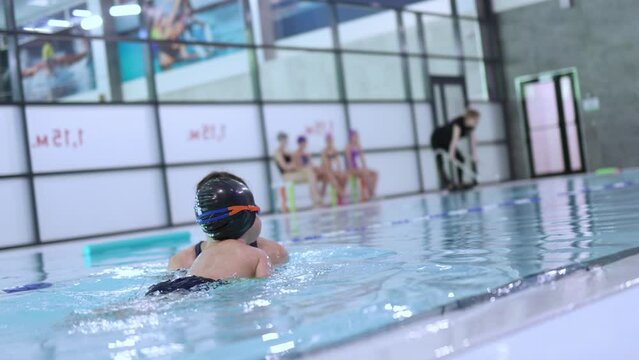 little baby boy child learning to swim with female coach trainer teacher in swimming pool. children swimming class for beginners. first training lesson teaching to float on water surface. kid goggles 