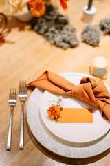 modern table serving for wedding in autumn style. orange flowers, autumn leaves, brown and orange napkins

