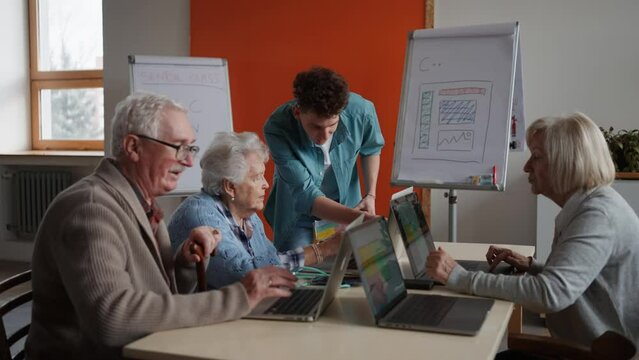 Senior group in retirement home with young instructor learning together in computer class