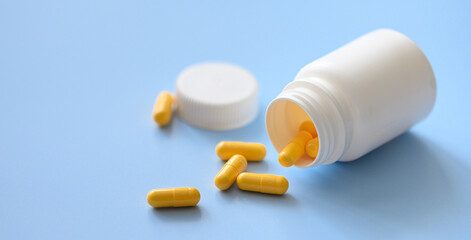 Yellow capsules scattered from white plastic medicine container