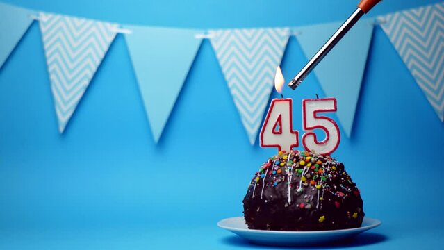 chocolate birthday cake with a burning candle number forty five, 45 on a blue background. Copy space. place for text.