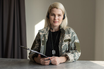 Sexy blond woman on army uniform posing at gray wall