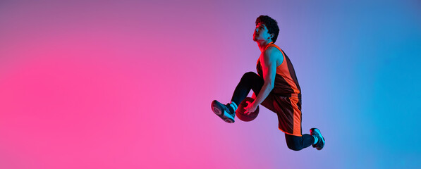 Fototapeta na wymiar Young energetic man playing basketball isolated on gradient pink blue studio background in neon light. Youth, hobby, motion, activity, sport concepts.
