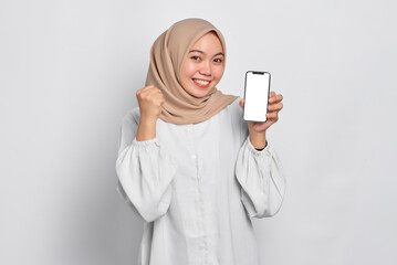 Excited young Asian Muslim woman showing mobile phone blank screen recommending App isolated over...