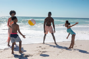 African american family enjoying summer holiday while playing with ball at beach on sunny day