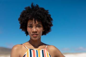 Portrait of confident young african american woman with afro hairstyle against blue sky