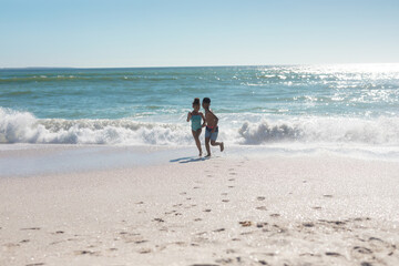 Full length of happy african american siblings playing together at beach against sky on sunny day