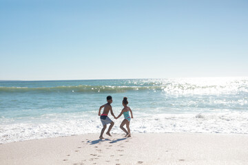 Full length of african american brother and sister holding hands while playing at beach on sunny day