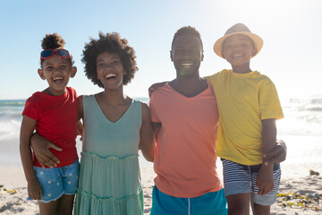 Portrait of smiling african american family with arms around enjoying summer holiday at beach