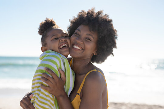 Portrait of cheerful african american mother and daughter with cheek to cheek at beach on sunny day