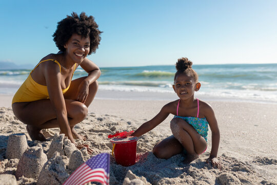 Portrait of smiling african american mother and daughter making sandcastles at beach
