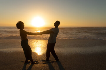 Full length side view of happy african american couple holding hands enjoying sunset at beach - Powered by Adobe