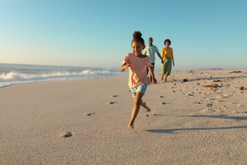 Happy african american girl running on sand against parents walking at beach
