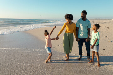 Happy african american family enjoying sunny day at beach against blue sky