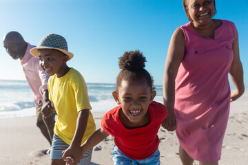 Happy african american grandchildren holding hands while pulling grandparents at beach