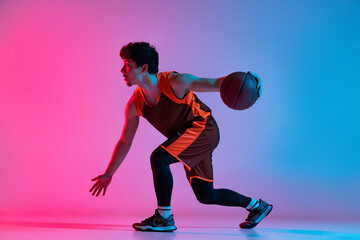 Sportive man playing basketball isolated on gradient pink blue studio background in neon light....
