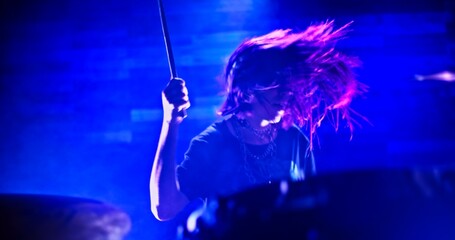 Close-up of girl emphatically playing the drums in twinkling strobe lights - obrazy, fototapety, plakaty