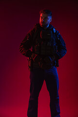 Fototapeta na wymiar airsoft player in full gear with guns GG RK74. a man in headphones, body armor, with a backpack and a belt. red background. colored, blue-red light