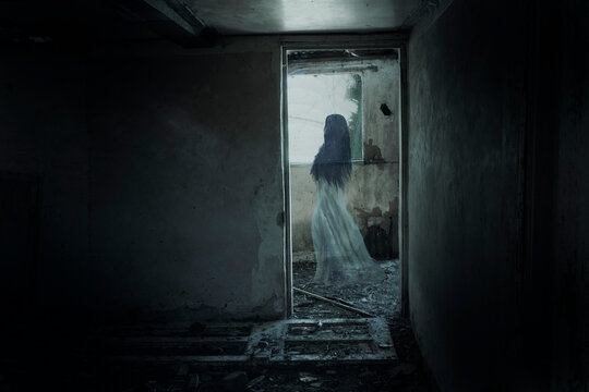 A woman ghost in a long dress floating past a doorway. In a haunted abandoned spooky house.