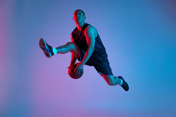 Fototapeta na wymiar Young sportive man playing basketball isolated on blue studio background in neon light. Youth, hobby, motion, activity, sport concepts.