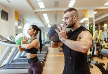 Fototapeta na wymiar Athletic man and woman are training together with medicine ball in modern gym. Healthy lifestyle
