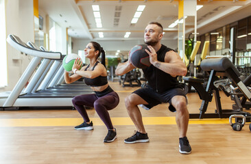 Athletic man and woman are training together with medicine ball in modern gym. Healthy lifestyle