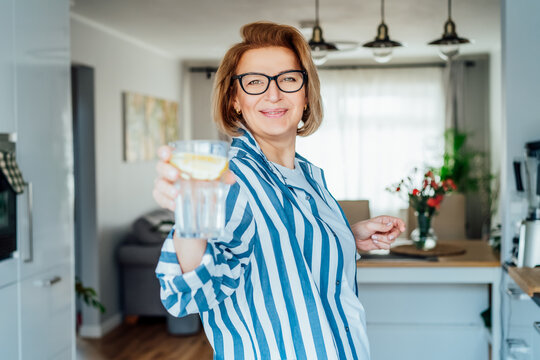 Healthy Habit To Drink Water. Smiling Middle Age Woman With Glass Of Pure Water With Lemon Standing On Her Kitchen. Control Body Hydration, Track Water Balance. Healthy Living. Selectivbe Focus.