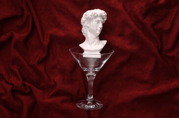Cocktail glass with David bust on red crumpled silk background. Party concept